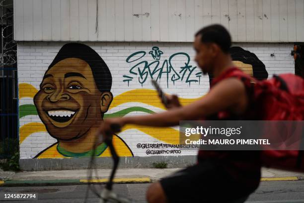 Man rides on a bike past a mural depicting Brazil's late football player Pele at Tijuca neighbourhood in Rio de Janeiro, Brazil, on December 29 just...