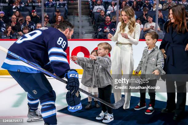 Sam Gagner of the Winnipeg Jets embraces his children Cali, Beckham and Cooper during the pre-game ceremony to commemorate his milestone 1000 career...