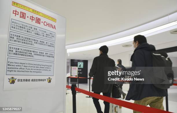 Passengers from Shanghai arrive at Narita airport near Tokyo on Dec. 30 with a notice board seen showing the Japanese government's new travel...