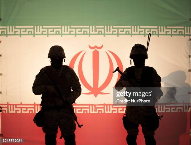 Two Islamic Revolutionary Guard Corps armed military personnel pose for a photograph in front of an Iran flag during a pro-government protest rally...