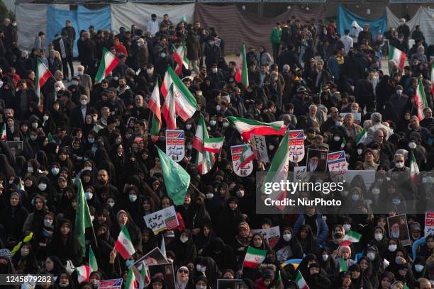 Veiled Iranian women hold Iran flags and placards while attending a pro-government protest rally in southern Tehran, December 29, 2022....