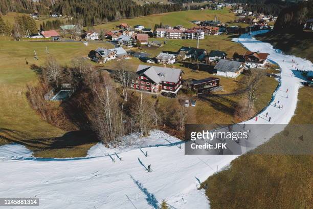 An aerial view taken on December 30, 2022 shows ski tourists making their way along a ski slope along meadows and houses in Riezlern, Austria. - Due...