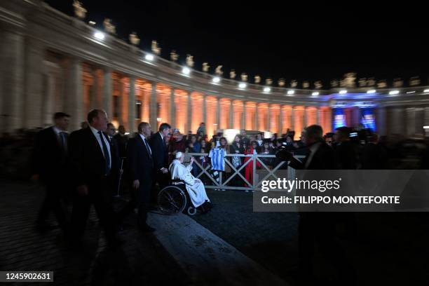 Pope Francis is flanked by officials as he waves to onlookers while moving in a wheelchair across St. Peter's Square in The Vatican on December 31,...