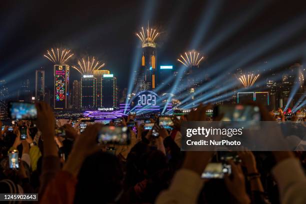 People watching Fireworks display over building on Hong Kong Island, 2023 display on the Hong Kong Convention and Exhibition Center to mark the...