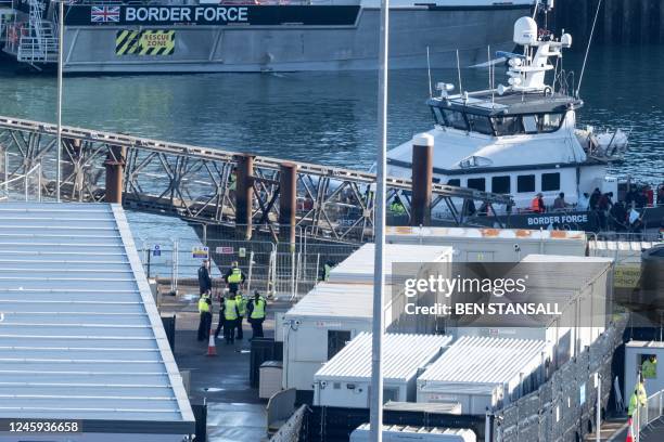 Migrants picked up at sea while attempting to cross the English Channel, are escorted off of the UK Border Force cutter 'BF Defender' at the Marina...