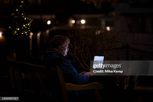 Person sitting on a bench working on a laptop at night with the light emanating from the screen lighting up their face on 7th December 2022 in...