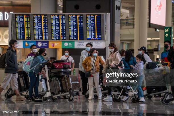 People with luggage standing in front of a flight information display board inside Terminal 1 of Hong Kong International Airport on January 2, 2023...