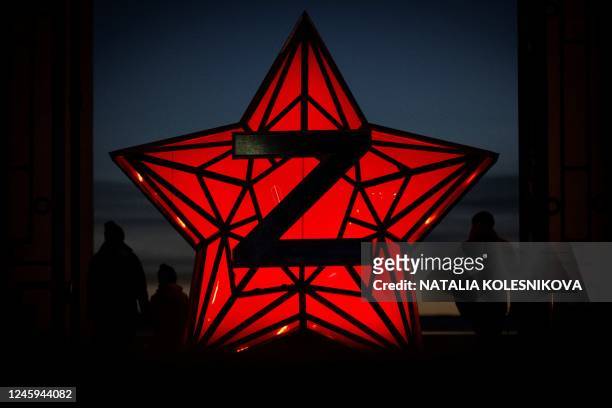 Pedestrians stand next to a New Year decoration stylised as the "Kremlin Star", bearing a Z letter, a tactical insignia of Russian troops in Ukraine,...