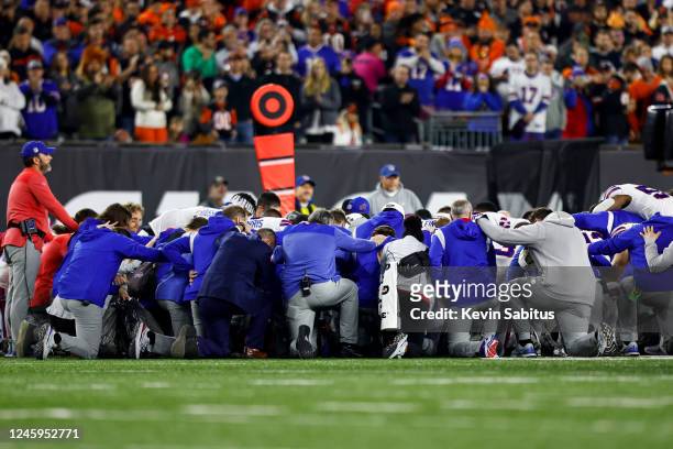 Buffalo Bills players and staff kneel together in solidarity after Damar Hamlin sustained an injury during the first quarter of an NFL football game...