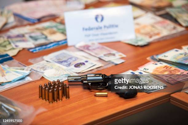 This photograph taken on January 3 shows a firearm and cash in various currency, displayed among other confiscated items at the Oost-Vlaanderen...