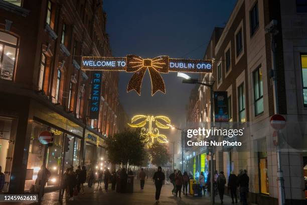 View of festive Christmas lights with 'Welcome to Dublin One' sign on busy Henry Street at night