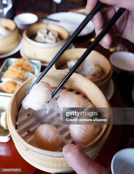 January 2023, Hamburg: A man reaches with chopsticks for dim sum, steamed dumplings, in a bamboo basket at the Chinese restaurant "Dim sum Haus". The...