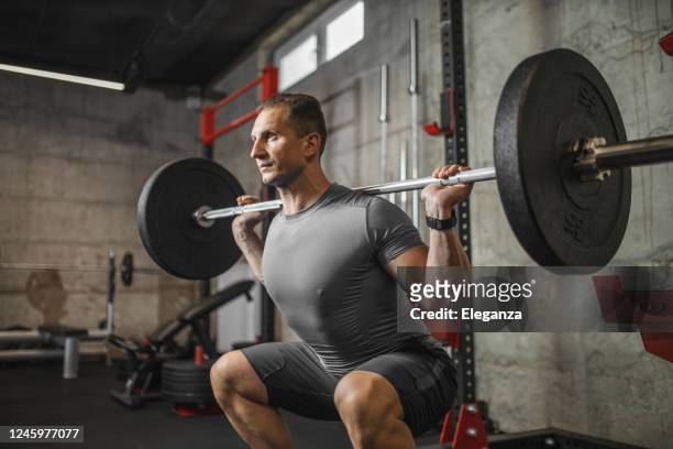 guapo hombre musculoso haciendo ejercicio en cuclillas con barbell en el gimnasio - hombre agachado fotografías e imágenes de stock