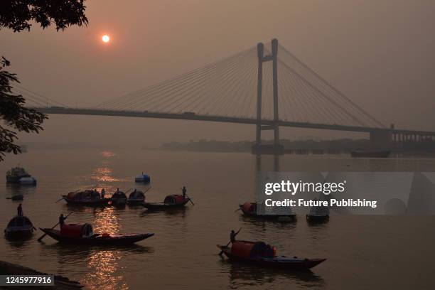 People travel in their boats during the last sunset across the Howrah Bridge On River Ganges. Scenic beauty of the setting sun on the last day of the...