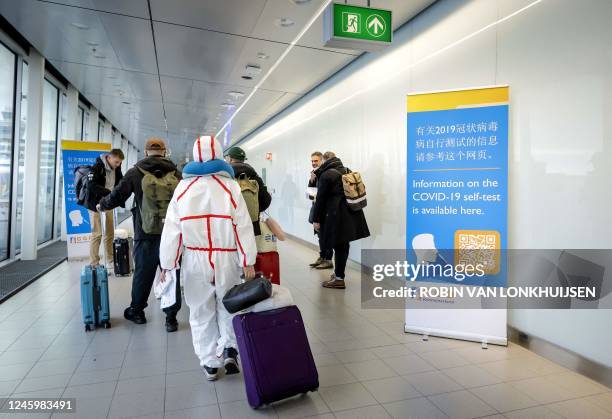 Travelers arriving China walk past information banners and receive free Covid-19 self-test kits, at Amsterdam's Schiphol Airport on January 4, 2023....