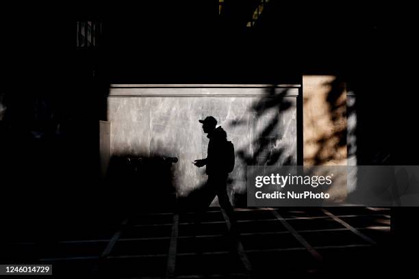 Man is walking wearing a hat and holding his smartphone in Athens, Greece on January 5, 2023.