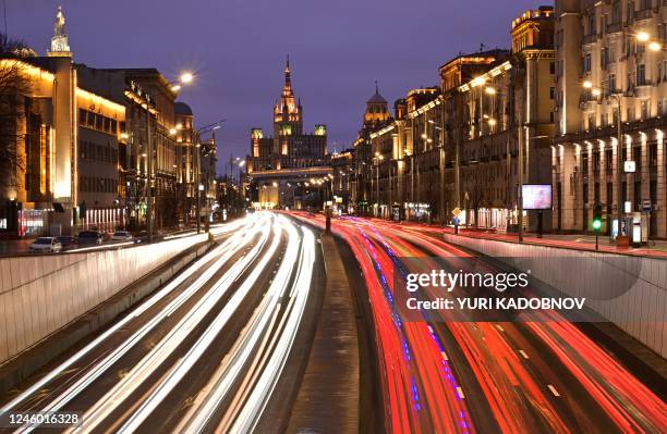 This photograph taken on January 5, 2023 shows car passing along a street leaving a light trails in front of a Stalin-era building in Moscow.