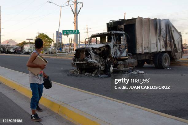 Man passes by a burnt truck on a street during an operation to arrest the son of Joaquin "El Chapo" Guzman, Ovidio Guzman, in Culiacan, Sinaloa...