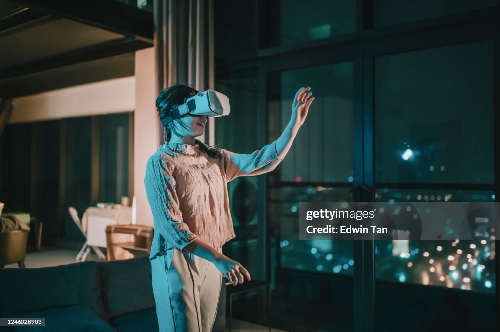 Une fille chinoise asiatique d’adolescent a mis sur des lunettes de VR et éprouvant l’expérience de jeu virtuel 3D dans le salon