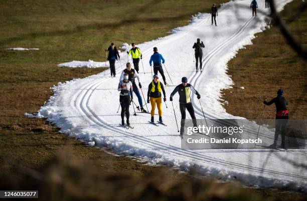 Cross-country skiers make their way on a cross-country ski run covered in artificial snow as grass covers the rest of the meadow on either side on...