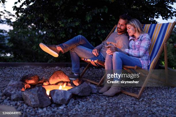 young loving couple relaxing in deck chairs by the bonfire. - warming up stock pictures, royalty-free photos & images
