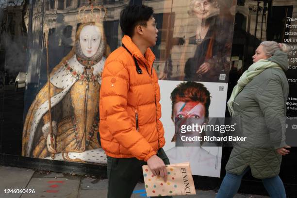 Members of the public walk past reproductions of Queen Elizabeth I, Emmeline Pankhurst and David Bowie printed on construction hoardings that...