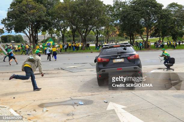 Supporters of Brazilian former President Jair Bolsonaro attack a vehicle of the Military Police during clashes outside Planalto Presidential Palace...