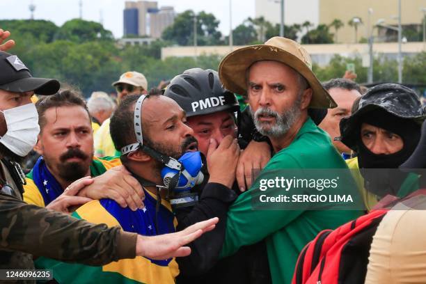 Supporters of Brazilian former President Jair Bolsonaro assist a Military Police officer during clashes after an invasion to Planalto Presidential...