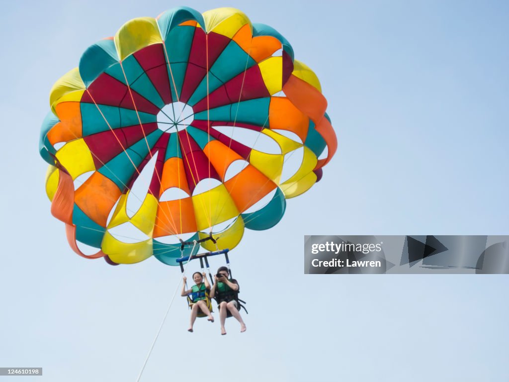 Couple are parasailing in sky.
