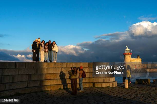 Young people are photographed in the port of Howth with the old lighthouse in the background, Howth is a population center in the administrative...