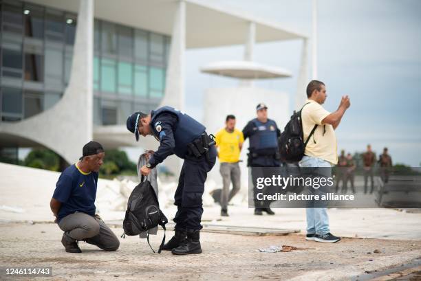 January 2023, Brazil, Brasilia: A police officer examines a man's backpack while another police officer escorts an arrested supporter of former...