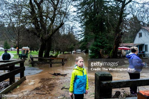 With flooded homes behind, a family begins to walk up along a covered bridge just above the overflowing Lorenzo River near the Felton Grove...