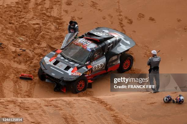 Audi's hybrid Spanish driver Carlos Sainz and co-driver Luca Cruz inspect their car after a crash during Stage 9 of the Dakar 2023 rally between...