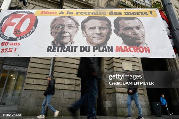 Pedestrians walk past a banner bearing portraits of Prime Minister Elisabeth Borne, President Emmanuel Macron and Labour Minister Olivier Dussopt and...