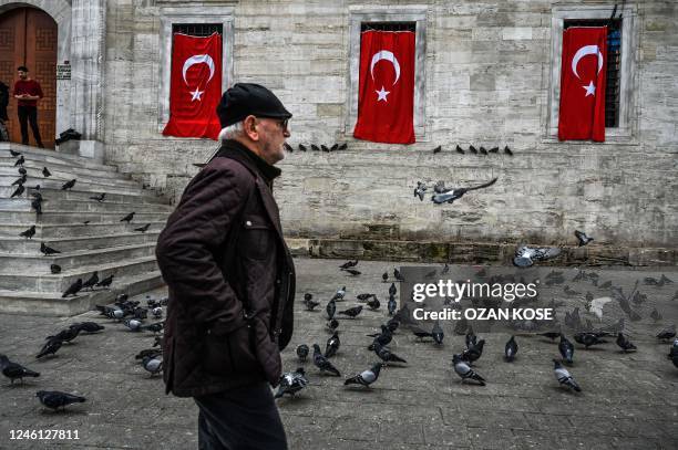 Pedestrian walks past pigeons in front of the New Mosque in the Eminonu district in Istanbul, on January 10, 2023.