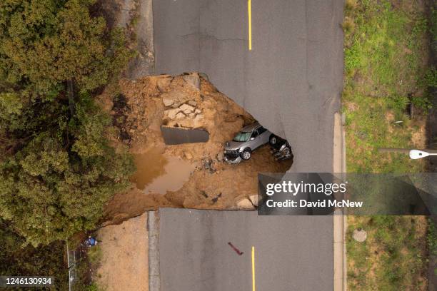 In an aerial view, a car and a pickup truck are seen inside a sinkhole as another storm created by a series of atmospheric rivers inundates...