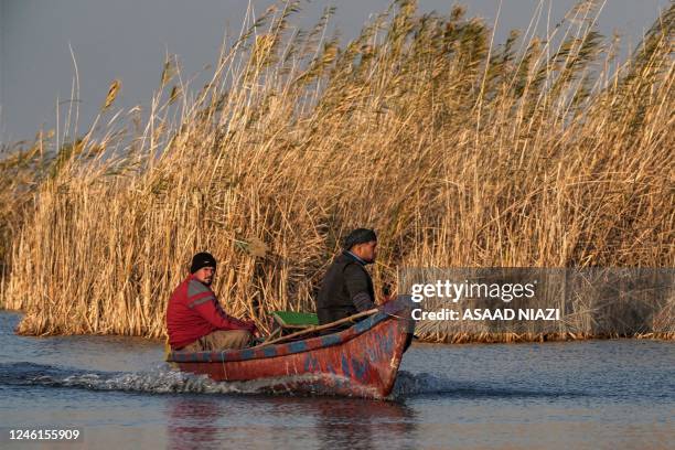 Men ride in a fishing boat cruising in the water in Iraq's southern marshes of Chibayish in Dhi Qar province on January 11, 2023.