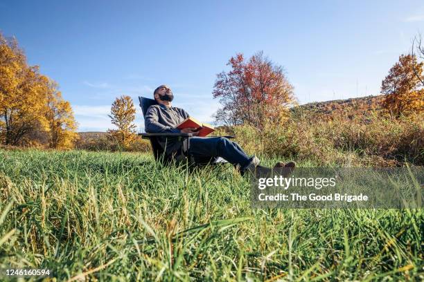 man relaxing in chair at grassy field - mann lässig gras sitzen stock-fotos und bilder