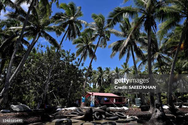 This picture taken on December 13, 2022 shows resident Lavenia McGoon with a family member standing past a makeshift seawall of old rubber car tyres...