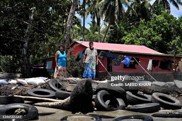 This picture taken on December 13, 2022 shows resident Lavenia McGoon with a family member standing past a makeshift seawall of old rubber car tyres...