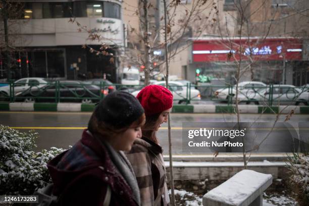 Two Iranian young women walk along a street-side in downtown Tehran on a snowy day, January 11, 2023. After days of air pollution in Tehran, Iranians...