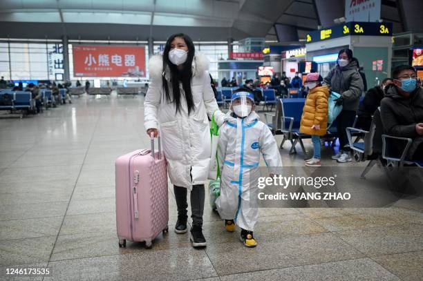 Woman leading child with personal protective equipment walk at a railway station in Beijing on January 12 as the annual migration begins with people...