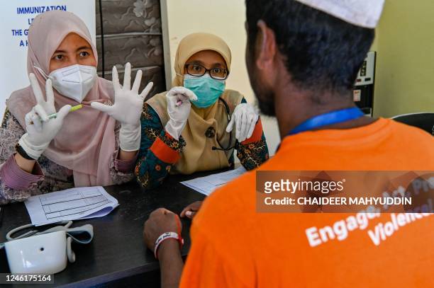 Health workers gesture as a Rohingya refugee receives a medical check-up at a temporary shelter in Ladong, Aceh province on January 12, 2023. -...