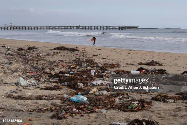 Seal Beach, CA A boogie boarder heading out to ride big waves walks past rash and debris covering a portion of the beach after recent storms brought...