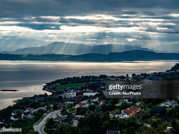 View of the first rays of Summer sunlight, over a small town close to a lake, in Norway, on June 24th, 2022.