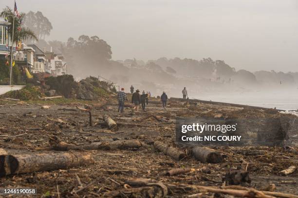 People walk on Rio Del Mar beach, covered with storm debris, in Aptos, California on January 12, 2023. - A "relentless parade of cyclones" hitting...