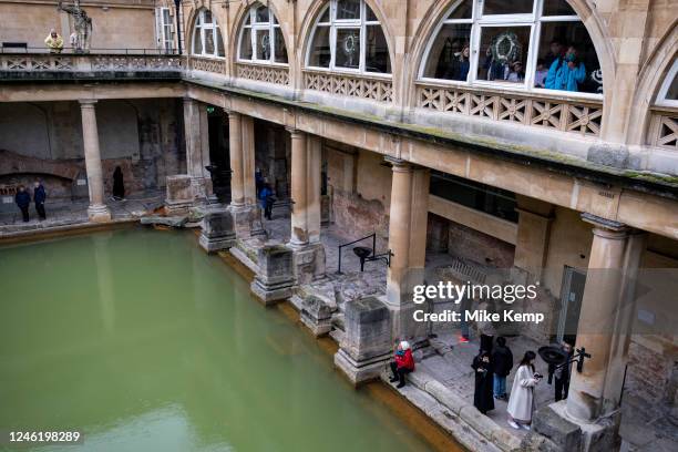 Tourists exploring the centrepiece at the Roman Baths, the Great Bath, and enjoy the columns, niches and steps surrounding the hot spring pool on...