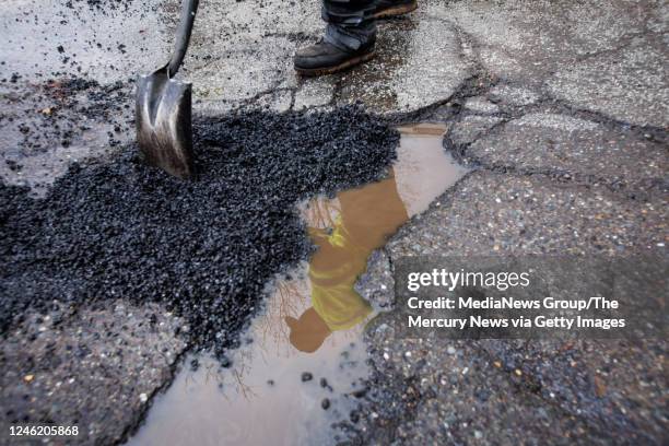 City of San Jose Department of Transportation maintenance worker Jose Quintero is reflected in a puddle as he fills potholes on Phelan Avenue in San...