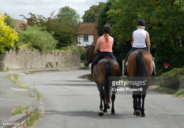two women hacking out through a village - recreational horseback riding 個照片及圖片檔