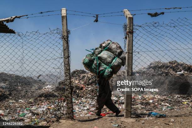 Waste picker carries bags with waste for recycling next to burning garbage at the Nakuru main dumping yard. Since waste is rarely segregated and is...